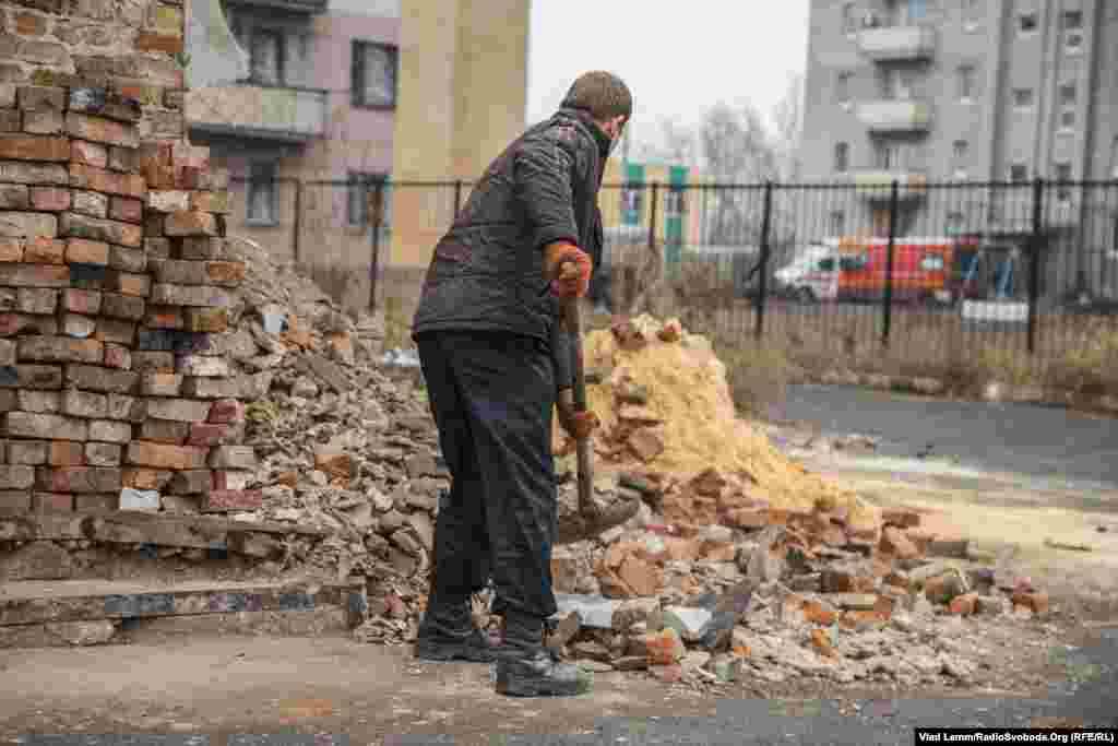 Несмотря на звук взрывов со стороны поселка Опытное, коммунальщики убирают листья с улиц. Этот местный житель убирает остатки битого кирпича